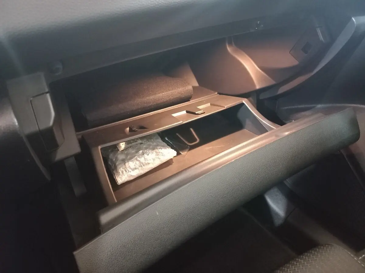 Gros plan sur la boîte à gants ouverte de la Renault Mégane Business gris foncé, montrant un rangement intérieur avec un objet emballé.