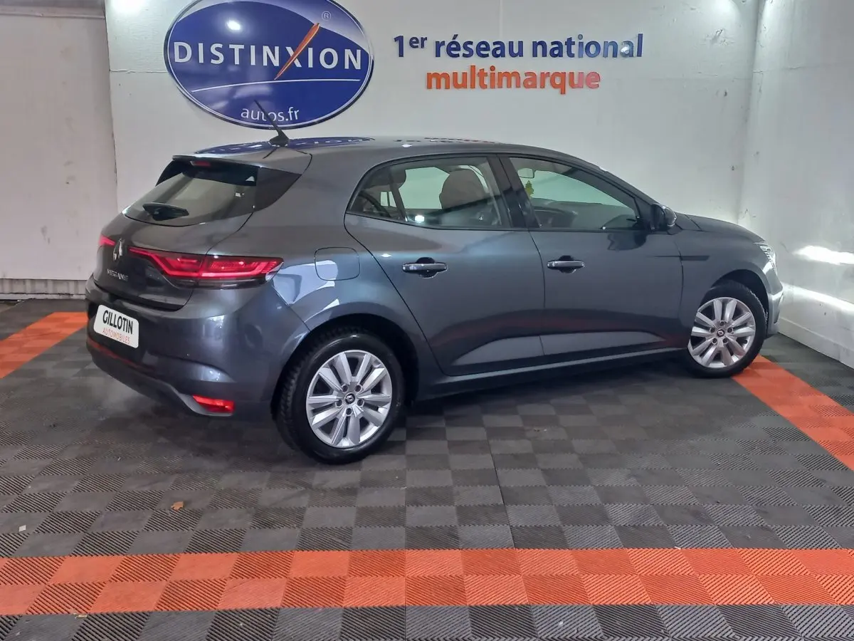 Vue 3/4 arrière droite d'une Renault Mégane Business TCe 115 gris foncé en intérieur avec feux arrière allumés.