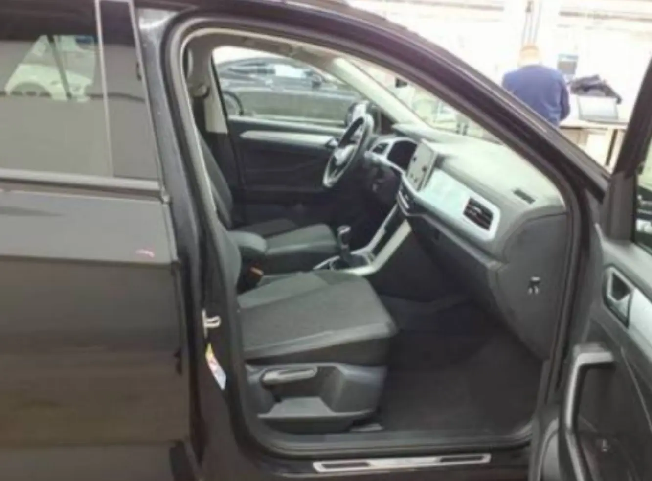 Vue intérieure côté conducteur d’un Volkswagen T-Roc noir 2025, montrant sièges tissu et tableau de bord moderne.