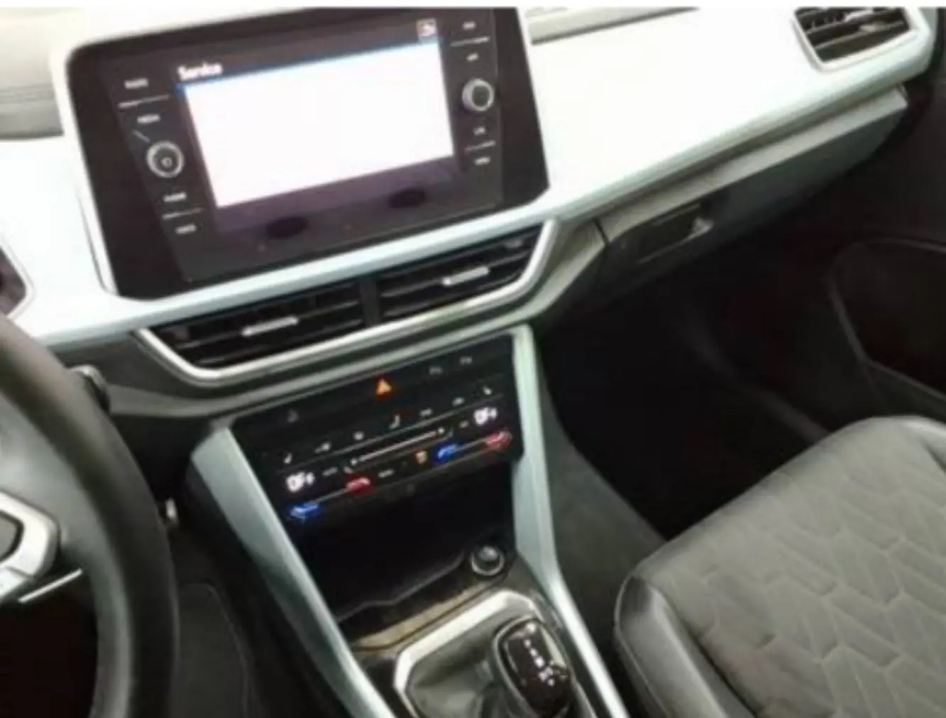 Vue intérieure du tableau de bord et console centrale du Volkswagen T-Roc 2025, avec écran tactile et sellerie tissu noir.