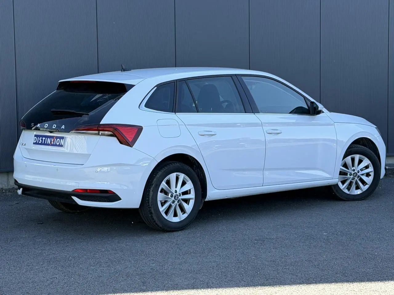 Vue 3/4 arrière droite d'une Skoda Scala blanc glacier avec lunette arrière surteintée et jantes alliage 16 pouces.