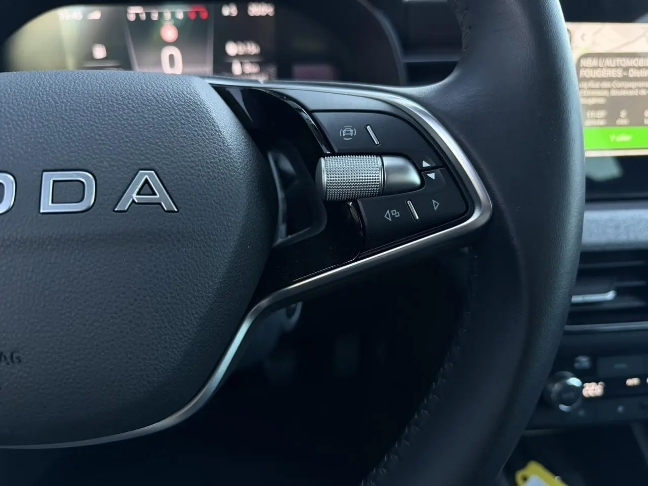 Gros plan sur le volant cuir noir multifonctions de la Skoda Scala TSI 116, avec commandes intégrées et tableau de bord numérique flou.