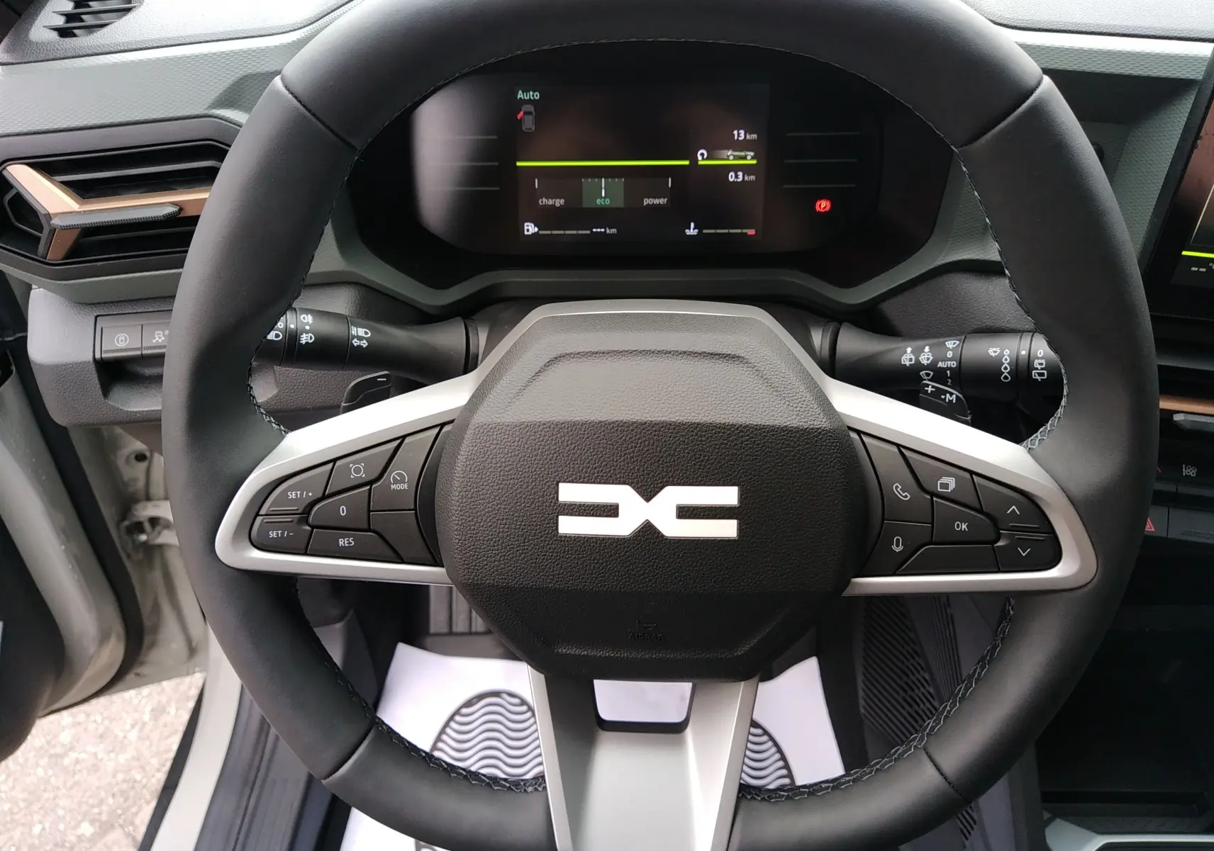 Vue rapprochée du volant noir avec logo DACIA stylisé et tableau de bord numérique du Dacia Duster Hybrid-G 2026.