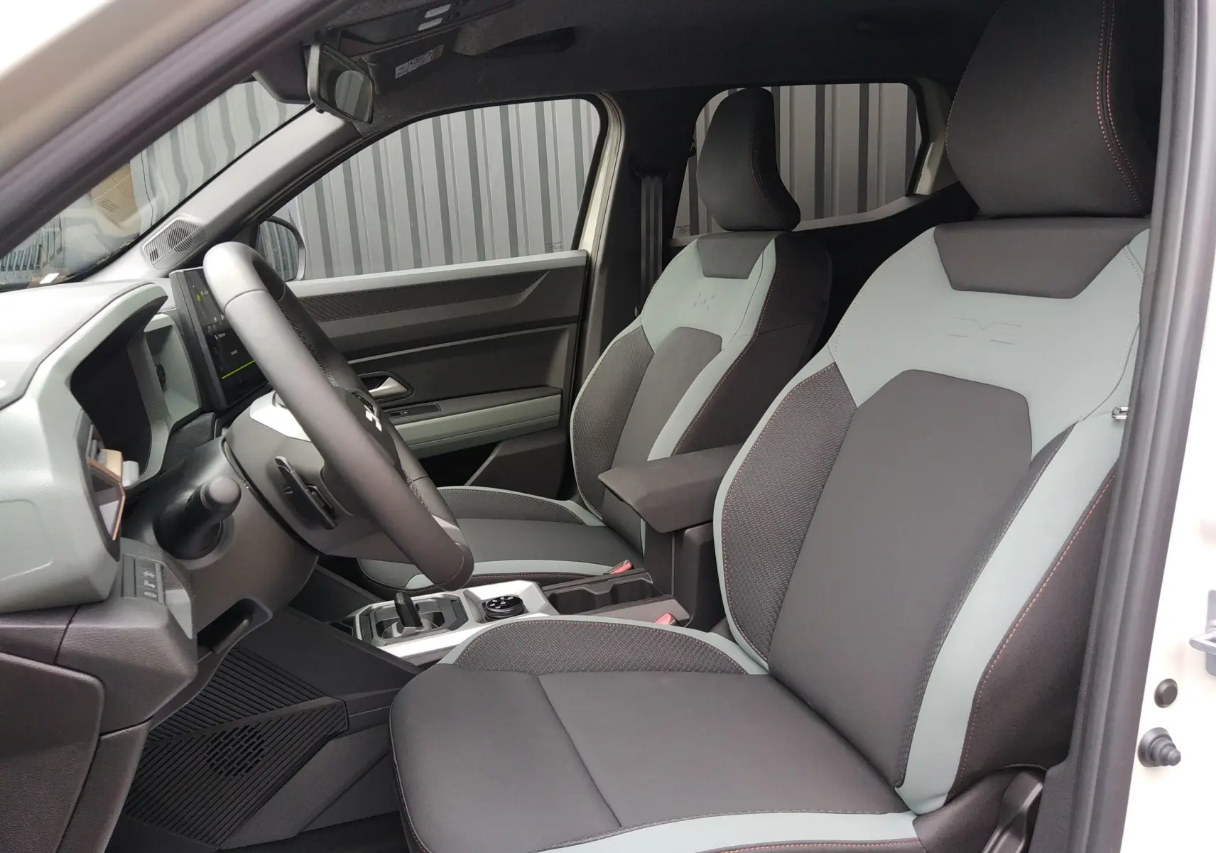 Vue intérieure côté gauche du Dacia Duster Hybrid-G 150 ch 4x4 Spirit of Sand avec sièges bicolores gris et noirs.