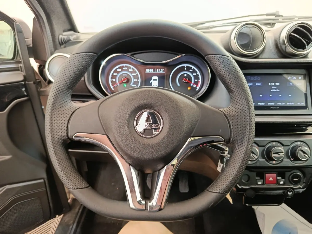 Vue rapprochée du volant noir perforé avec logo Aixam, tableau de bord et console centrale d'une Aixam Ambition blanche 2026.