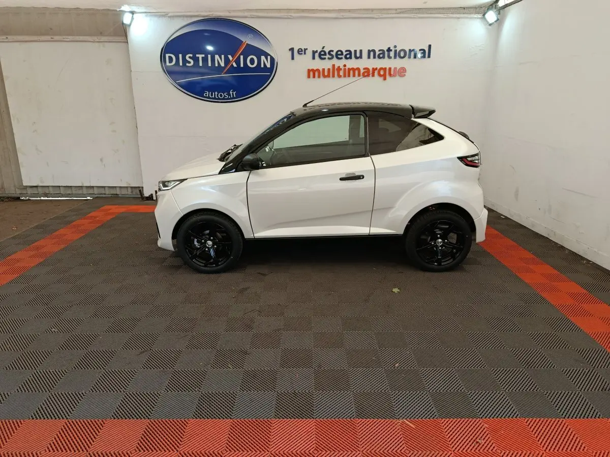Vue de profil côté gauche d'une Aixam Ambition 0.5 City Coupe Sport blanche avec jantes noires dans un showroom.