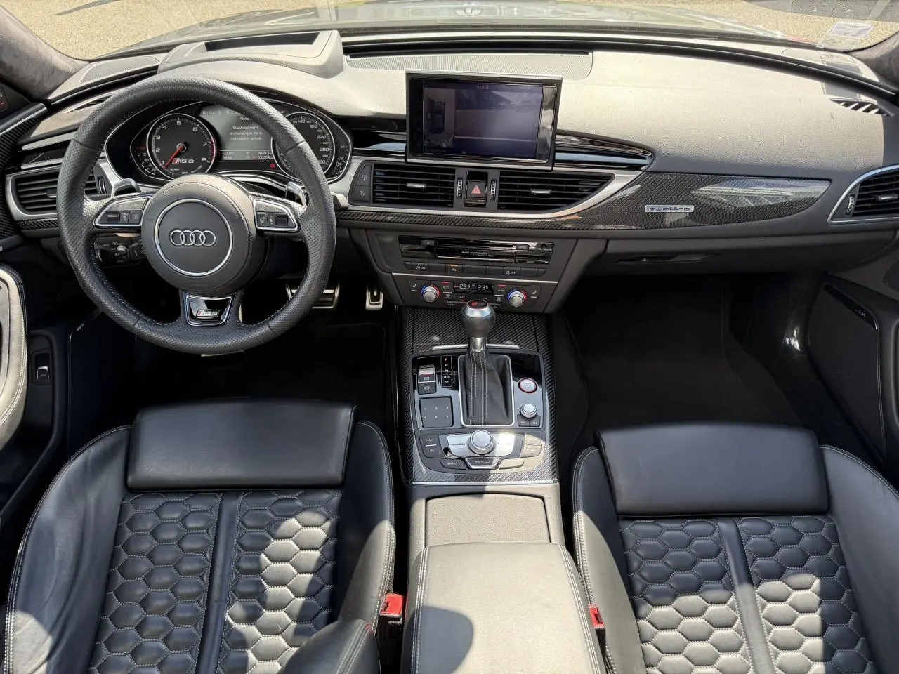 Vue intérieure avant de l'Audi RS6 Avant 2016 avec sellerie cuir noire à motif nid d'abeilles et tableau de bord carbone.