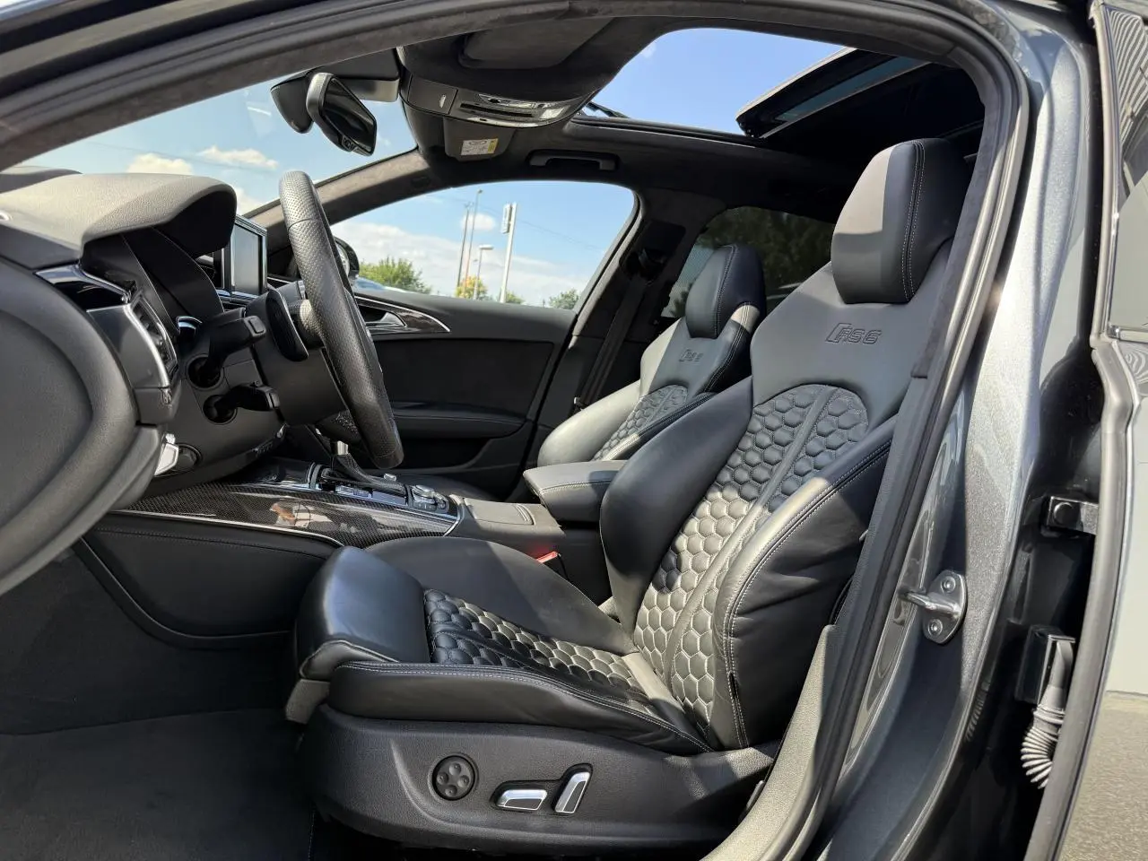 Intérieur avant droit de l'Audi RS6 Avant gris Daytona nacré, sièges sport en cuir noir embossé RS6 et toit ouvrant panoramique.