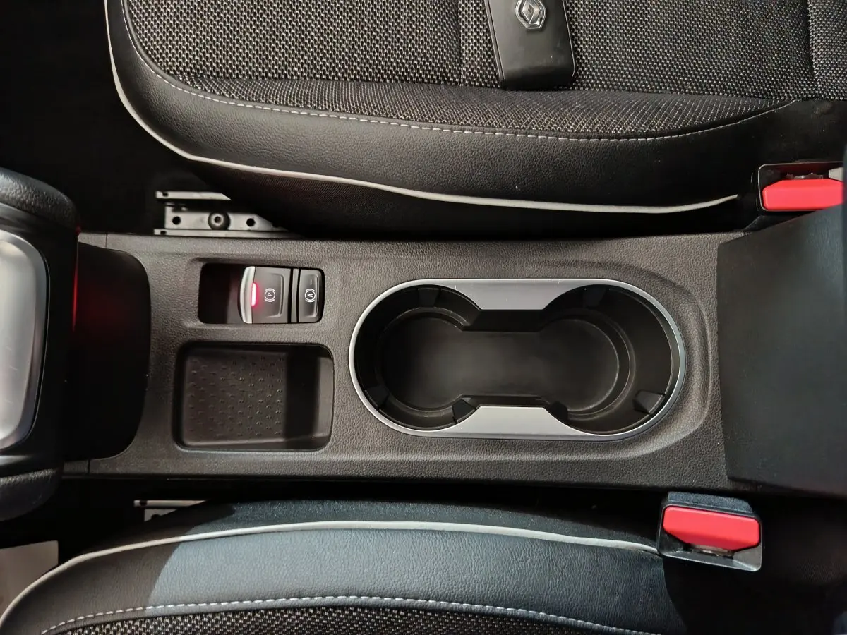 Vue plongeante sur la console centrale noire du Renault Captur 2024, avec porte-gobelets et bouton frein à main électrique.