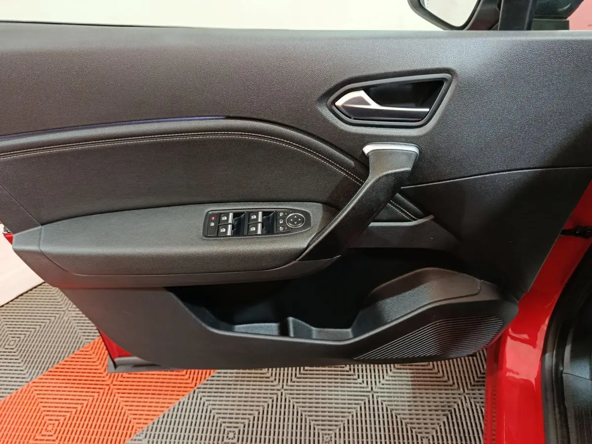 Vue intérieure côté gauche de la porte avant rouge du Renault Captur 2024 avec commandes de vitres et poignée noire.