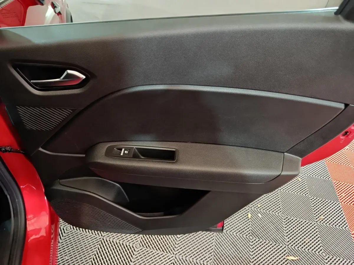 Vue intérieure côté gauche de la porte avant rouge du Renault Captur 2024 avec poignée et commande de vitre noire.