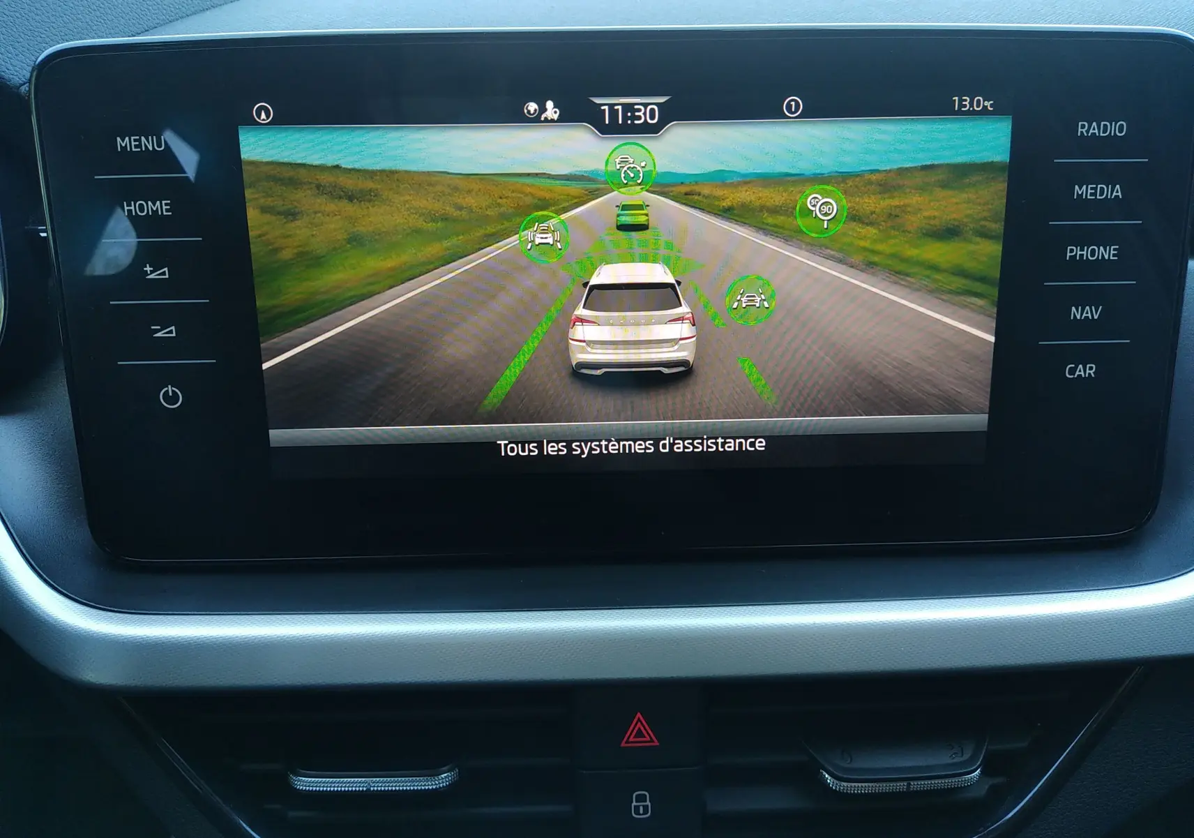 Écran central du Skoda Kamiq 2023 montrant l'affichage des systèmes d'assistance à la conduite avec vue arrière du véhicule gris.