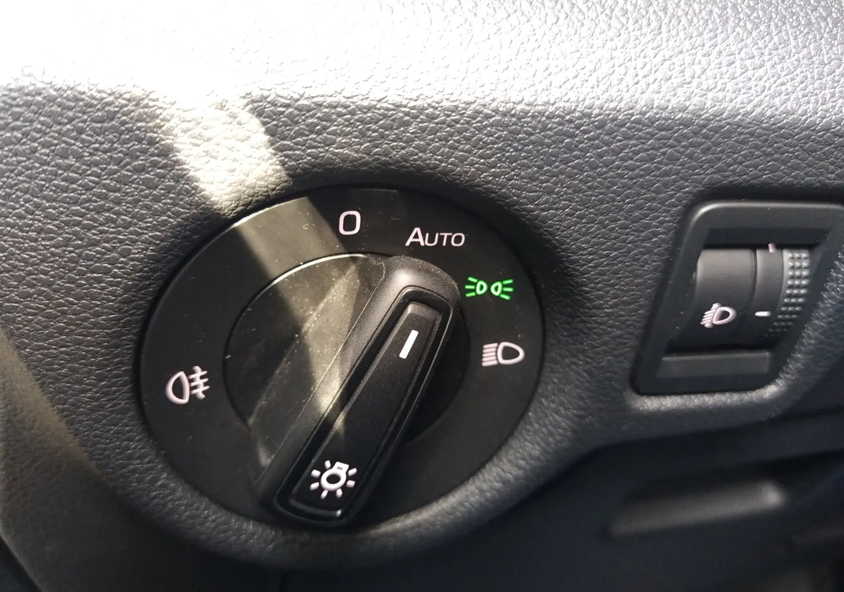 Gros plan sur le bouton de commande des phares du Skoda Kamiq 2023, avec réglage sur mode automatique et témoin vert allumé.