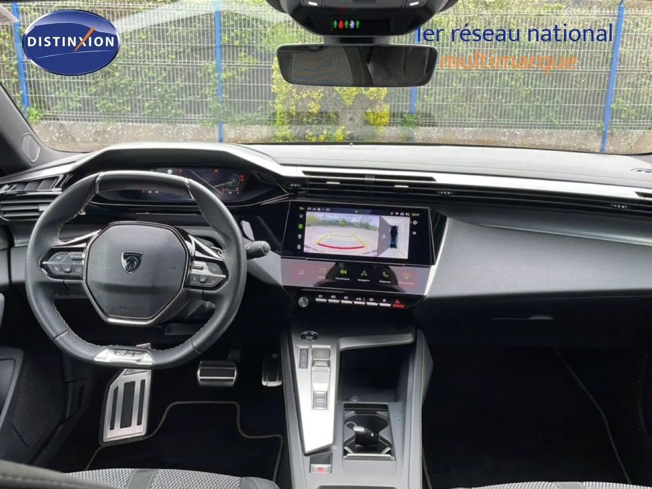 Vue intérieure avant du tableau de bord et volant noir de la Peugeot 408 1.2 Hybrid 145ch GT avec écran tactile affichant la caméra de recul.
