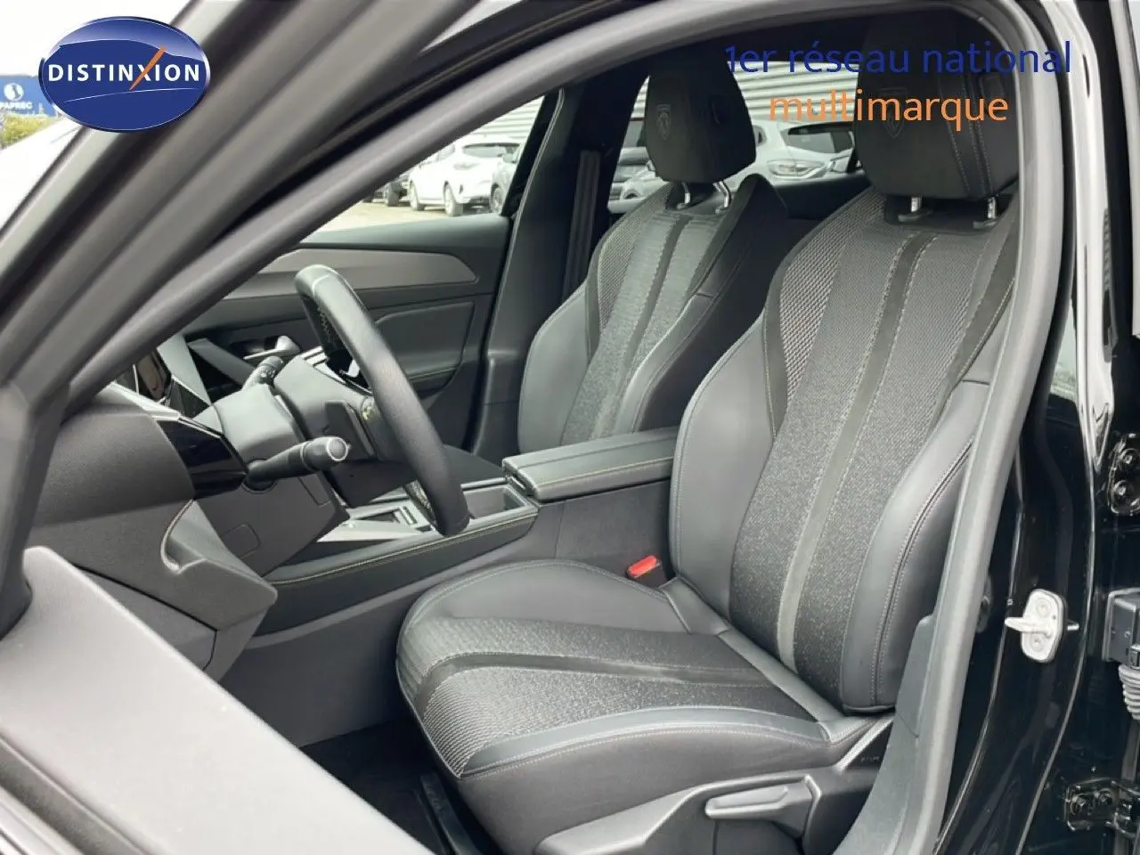 Vue intérieure côté conducteur de la Peugeot 408 2025 noire, mettant en valeur les sièges en tissu et cuir gris avec volant multifonction.