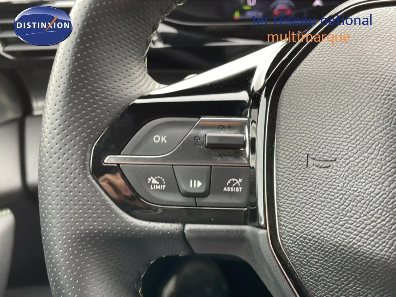 Gros plan sur le volant noir perforé de la Peugeot 408 1.2 Hybrid 145ch, avec commandes intégrées et finition brillante.