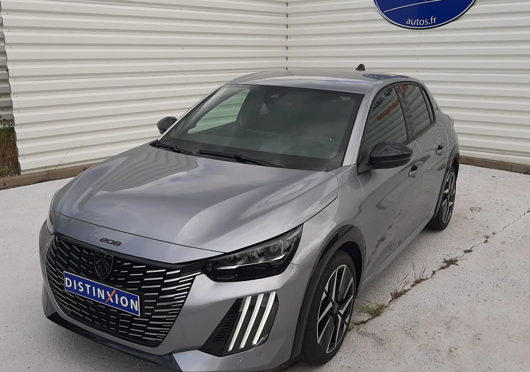 PEUGEOT 208 gris Artense en 3/4 avant droit, avec calandre noire et feux LED verticaux distinctifs.