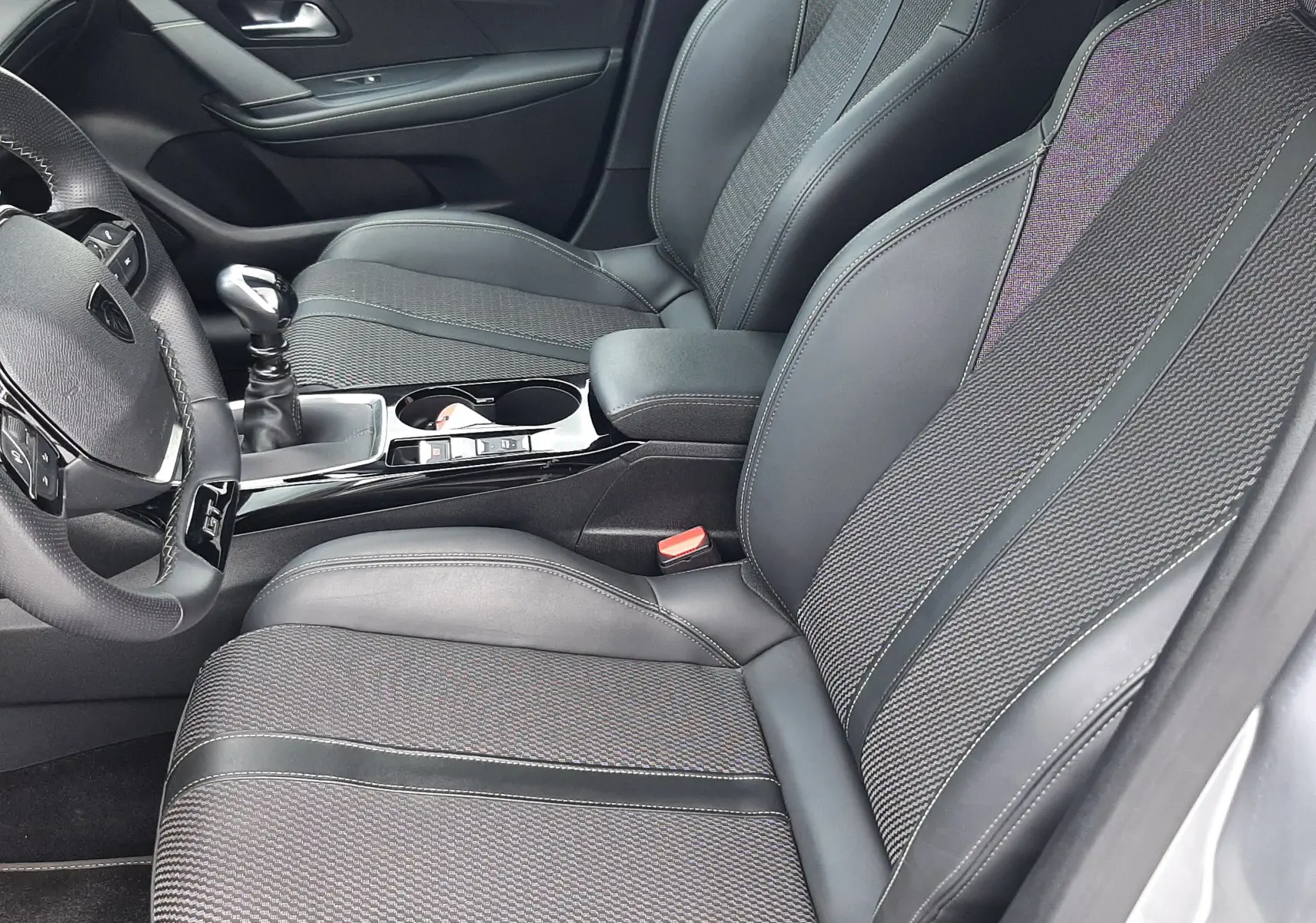 Vue intérieure côté conducteur de la Peugeot 208 1.2 GT 2025, sièges en tissu et cuir noir avec surpiqûres contrastées.