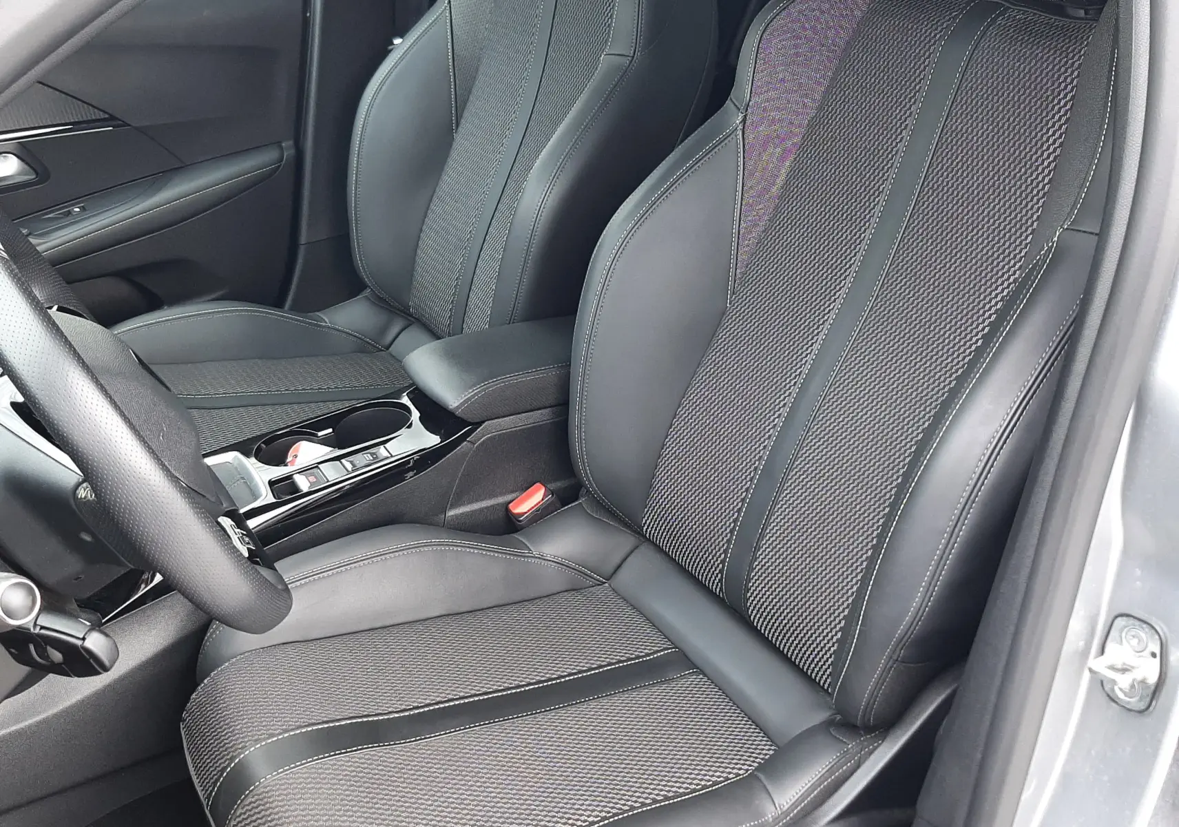 Vue intérieure côté conducteur de la Peugeot 208 GT 1.2 essence 2025, sièges tissu et cuir gris avec surpiqûres contrastées.