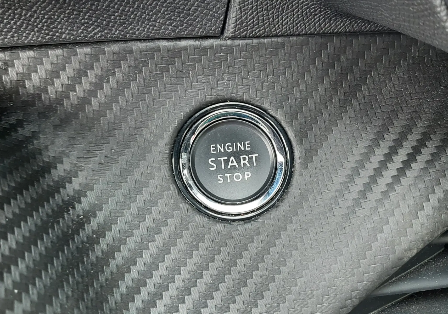 Bouton start/stop moteur sur tableau de bord effet carbone de la Peugeot 208 1.2 100CH S&S GT, intérieur noir.