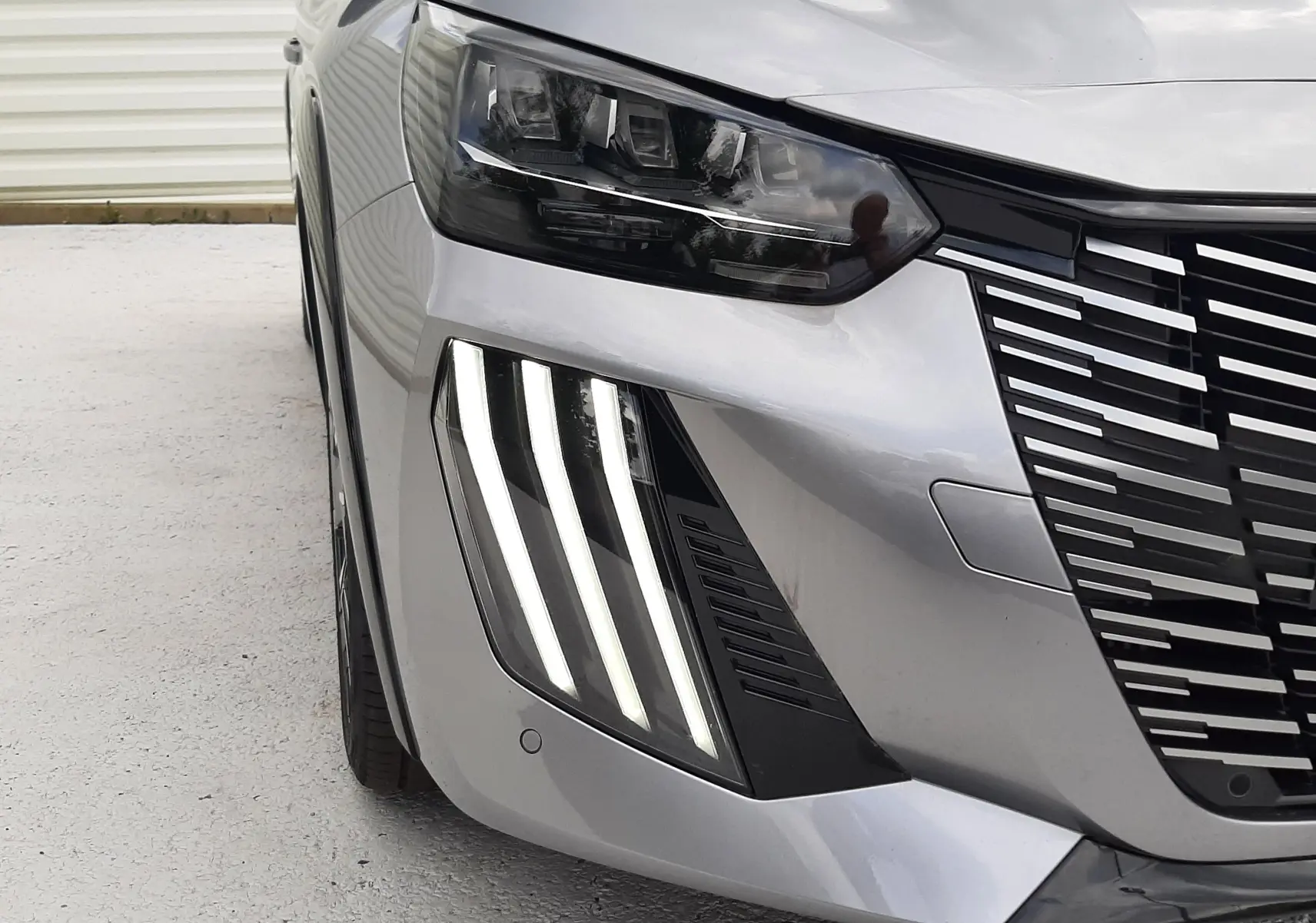 Gros plan sur l’avant droit d’une Peugeot 208 gris Artense, mettant en valeur les phares LED et la calandre distinctive.