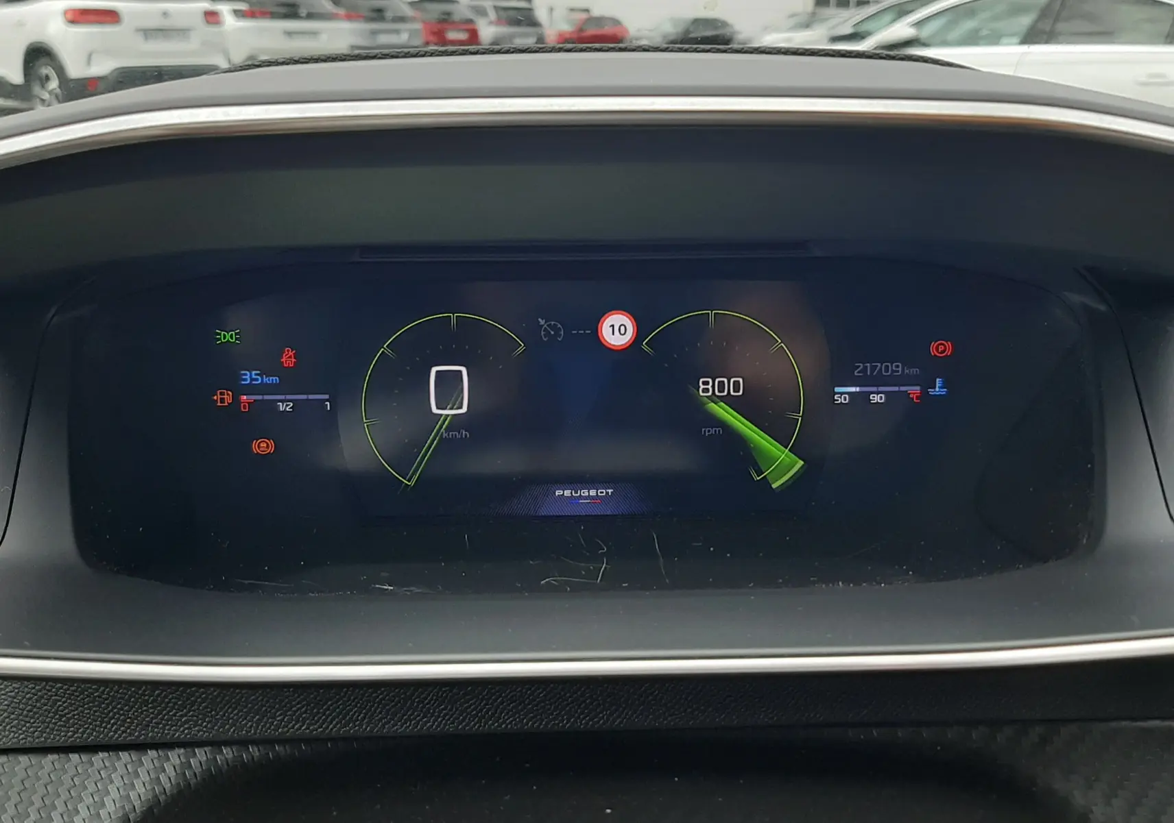 Tableau de bord numérique de la Peugeot 208 1.2 100CH GT, affichant vitesse, régime et alertes, vue frontale intérieure.