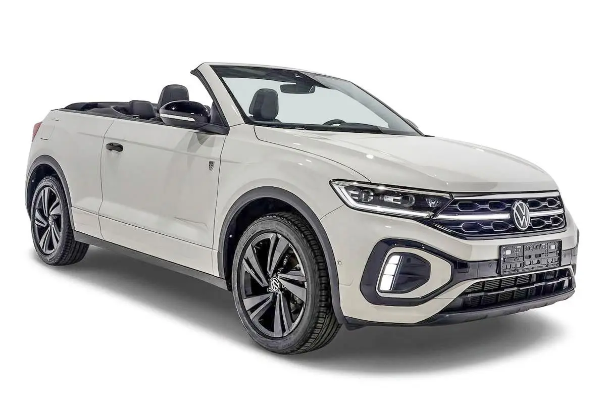 Vue 3/4 avant d’un Volkswagen T-Roc Cabriolet beige métallisé avec capote ouverte et jantes noires distinctives.