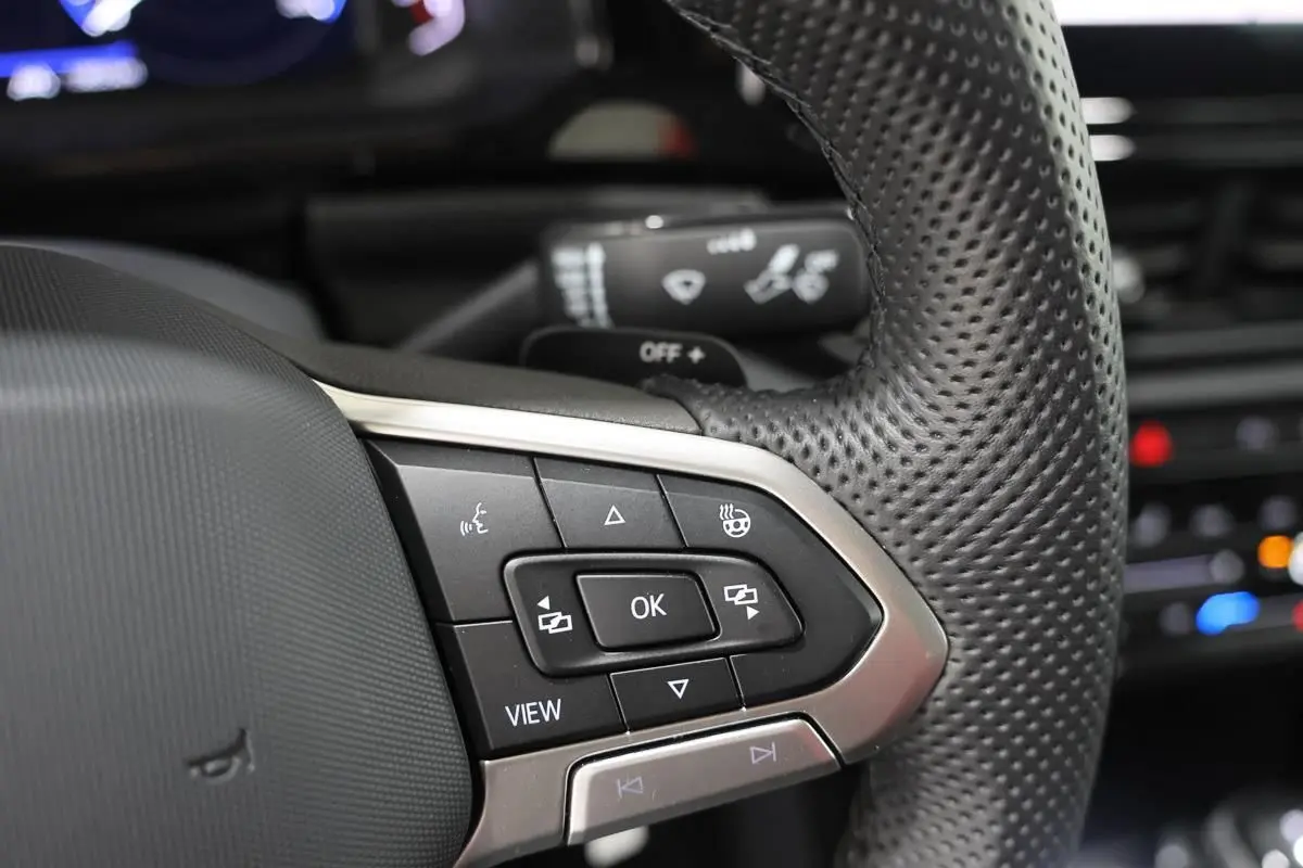 Gros plan sur les commandes multifonctions en cuir perforé du volant du Volkswagen T-Roc Cabriolet beige métallisé.
