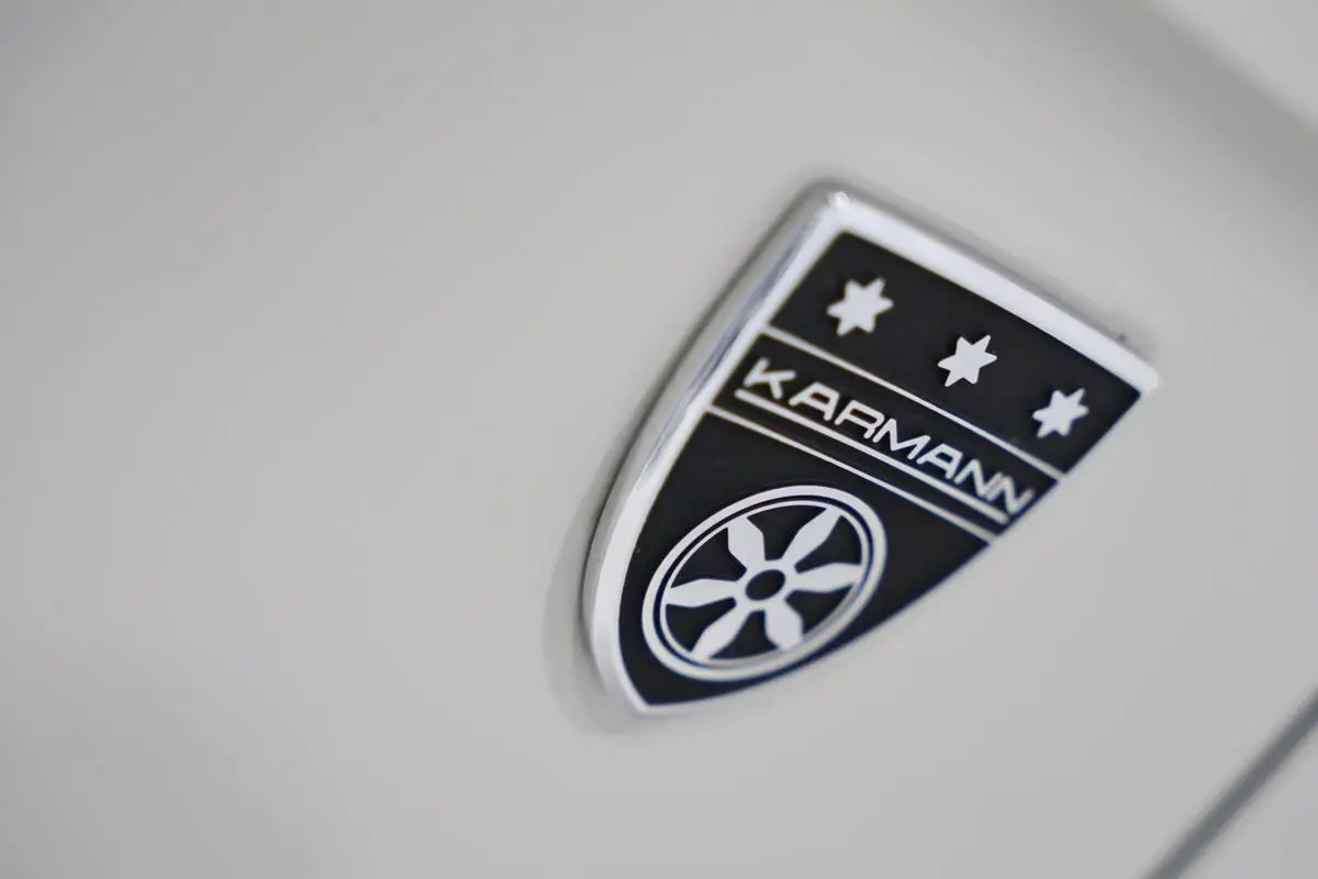 Gros plan sur l’écusson Karmann noir et argent sur la carrosserie beige métallisée du Volkswagen T-Roc Cabriolet.