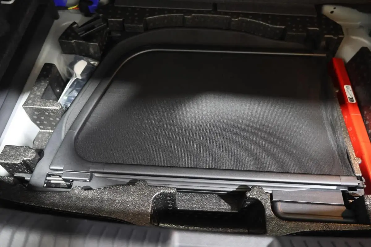 Rangement sous coffre montrant un filet de protection noir et des accessoires dans un Volkswagen T-Roc Cabriolet beige.