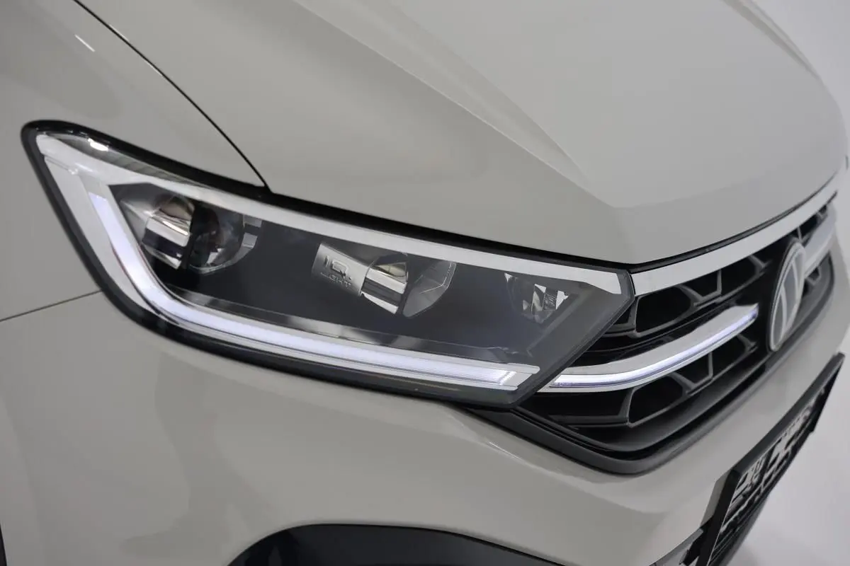 Gros plan sur le phare avant gauche et la calandre noire d’un Volkswagen T-Roc Cabriolet beige métallisé.