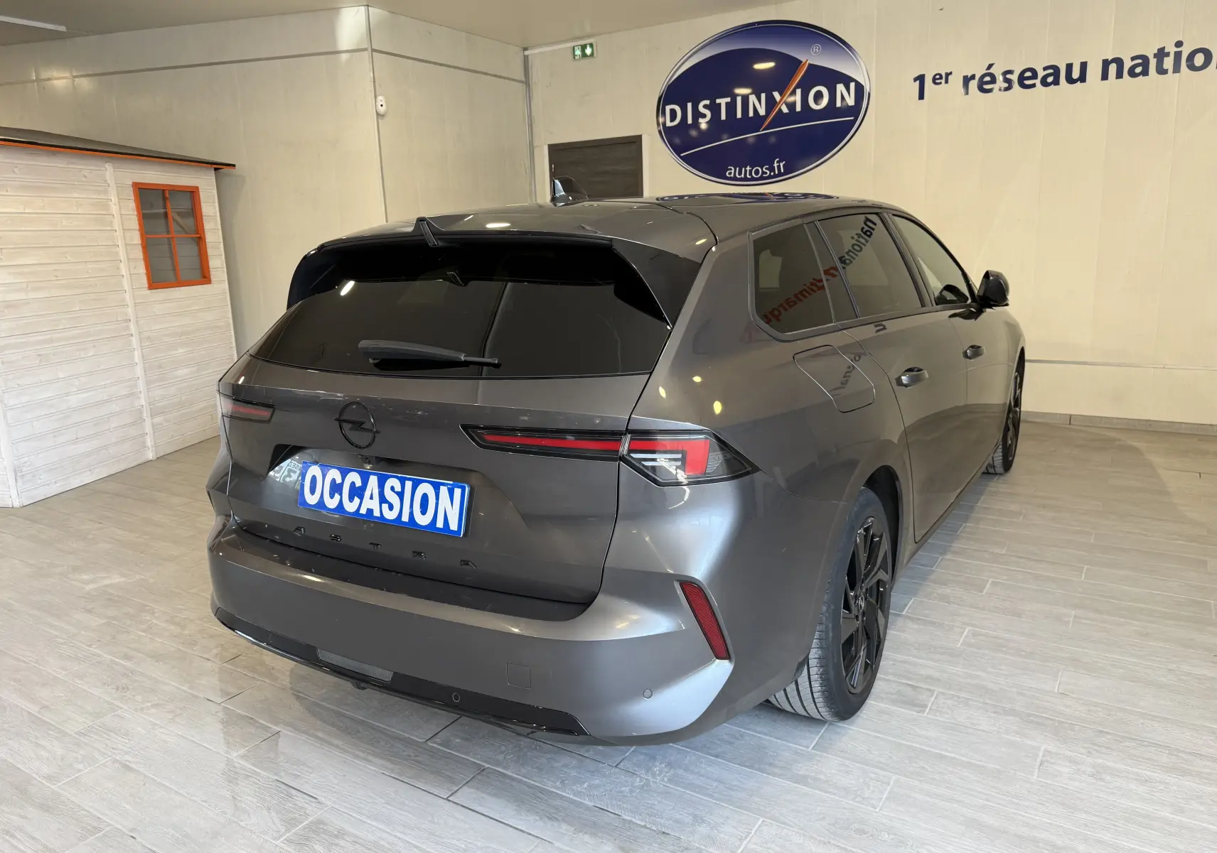 Opel Astra Sports Tourer gris vue 3/4 arrière droit en intérieur avec vitres teintées et jantes noires.