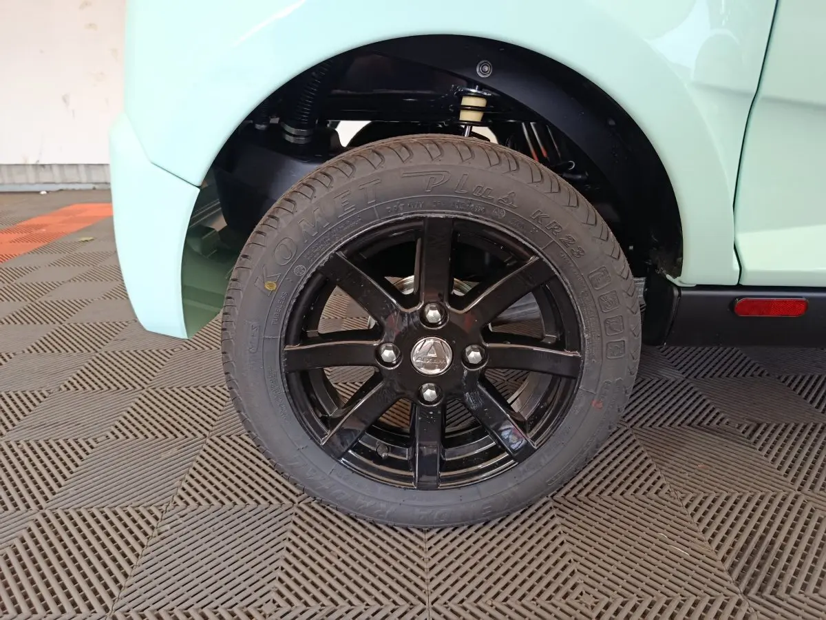 Gros plan sur la roue arrière droite noire de l'AIXAM AMBITION vert clair, avec logo central et suspension visible.
