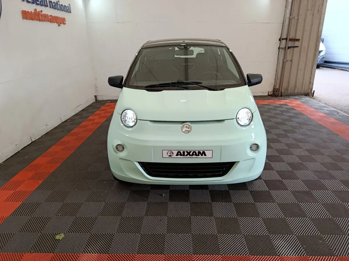 Vue frontale d'une Aixam Ambition Easy Chic thermique S10-2 2026 en vert clair avec toit noir dans un showroom.