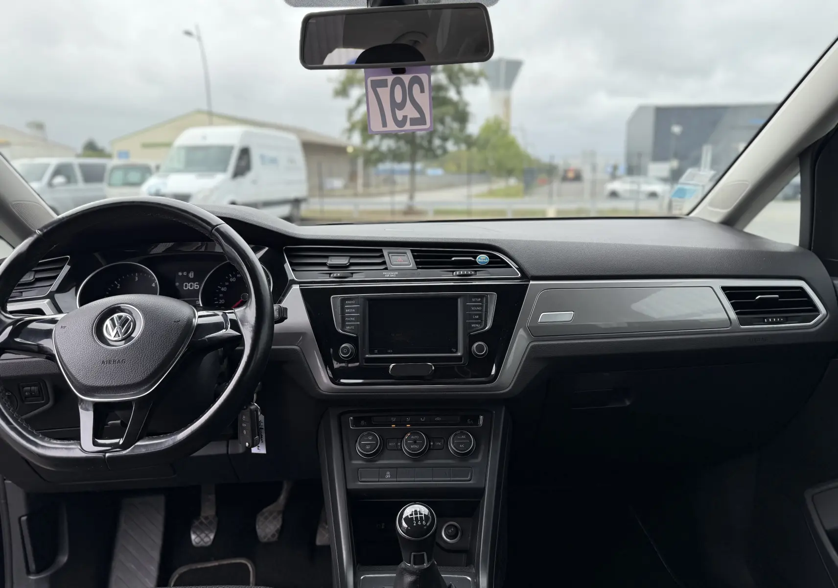 Vue intérieure frontale du Volkswagen Touran noir 2017, mettant en valeur le volant, la console centrale avec écran et la boîte manuelle.