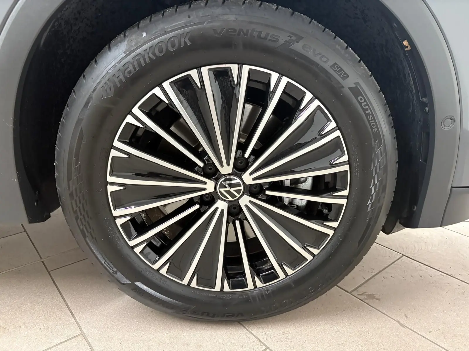 Gros plan sur la jante alliage bicolore du Volkswagen Tiguan Gris Dauphin, pneu Hankook visible sur sol carrelé.
