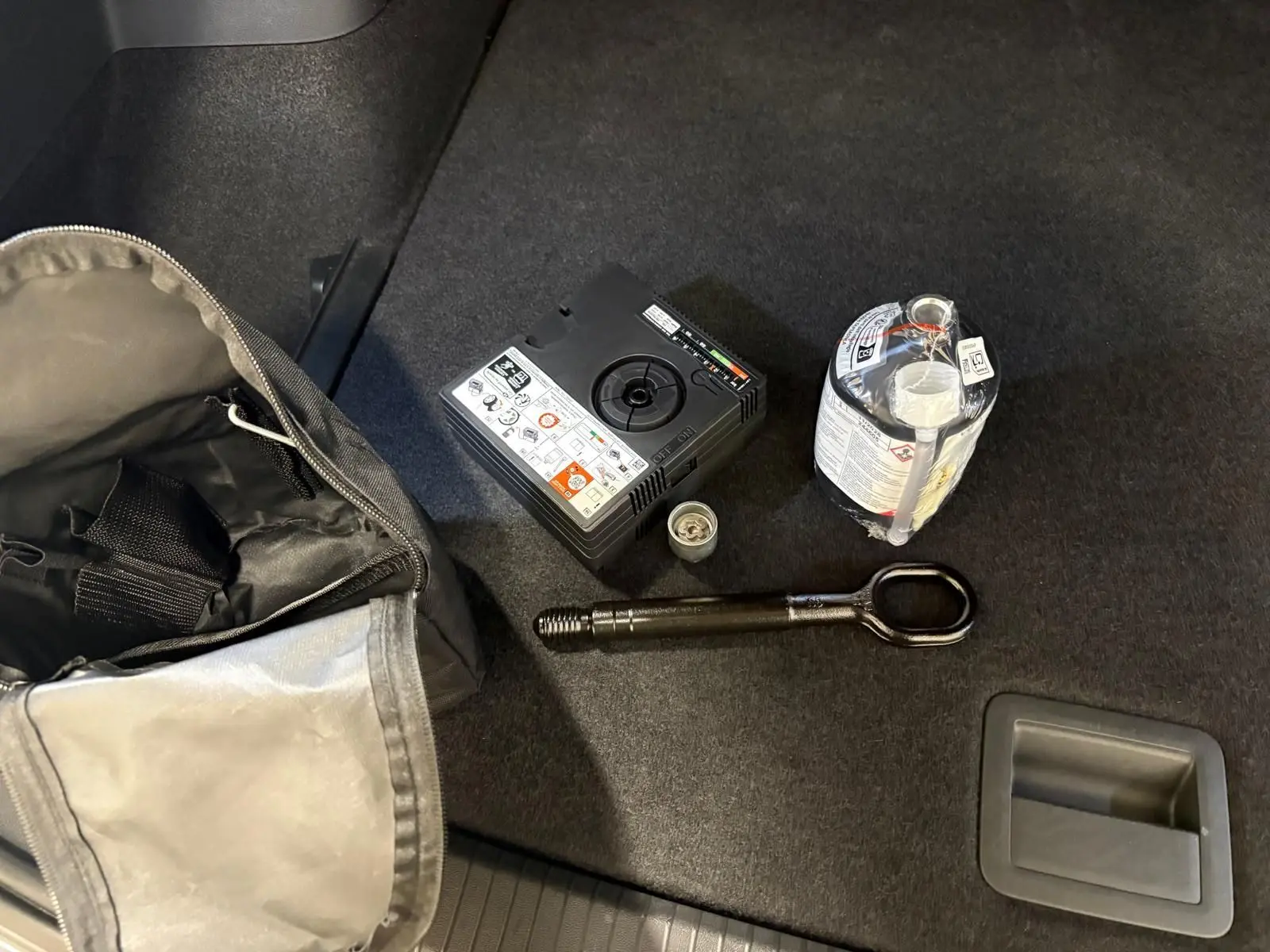 Vue rapprochée du coffre d’un Volkswagen Tiguan 2.0 TDI gris Dauphin, montrant les outils de dépannage rangés au sol.
