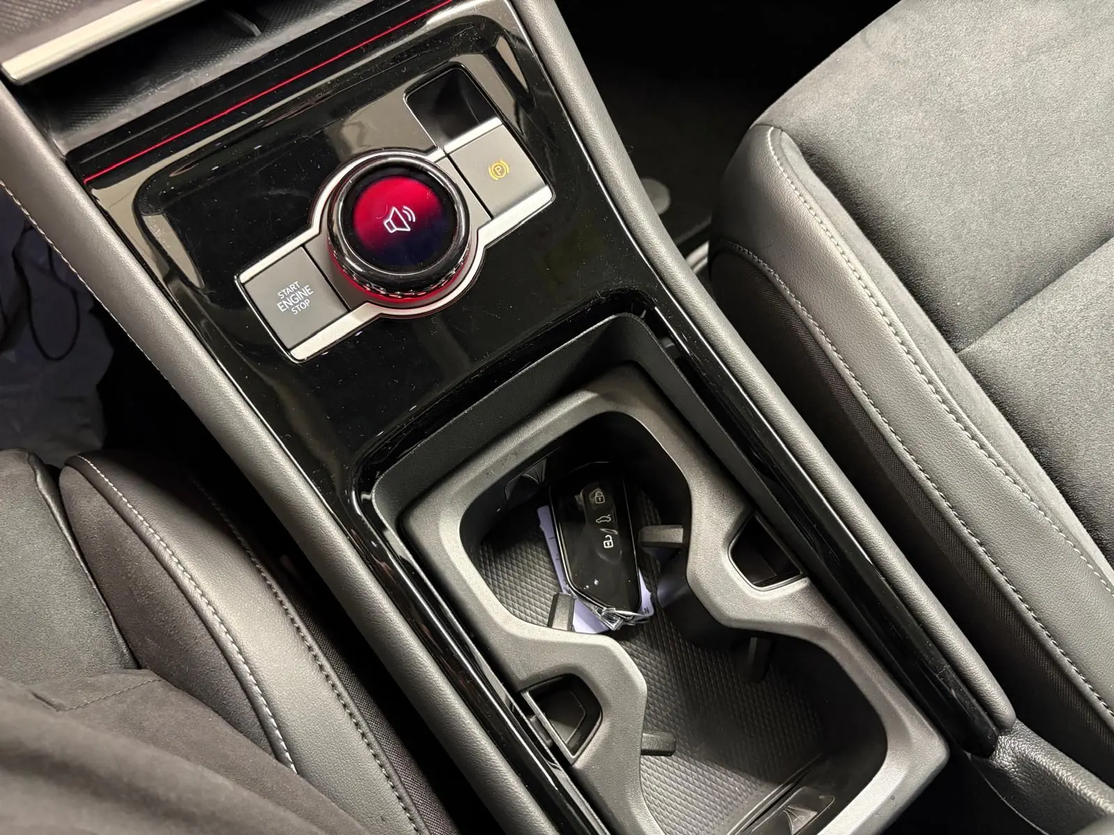 Gros plan sur la console centrale noire brillante du Volkswagen Tiguan 2025 avec bouton start/stop et porte-clés dans le porte-gobelets.