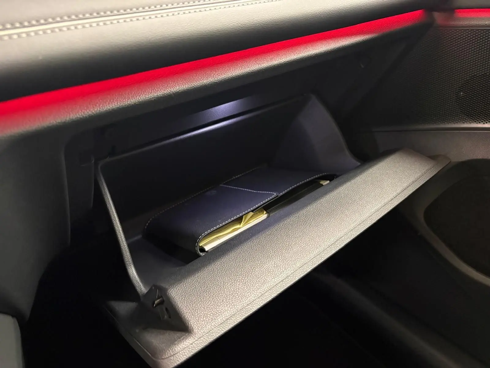 Gros plan sur la boîte à gants ouverte du Volkswagen Tiguan 2025, intérieur noir avec éclairage d'ambiance rouge.