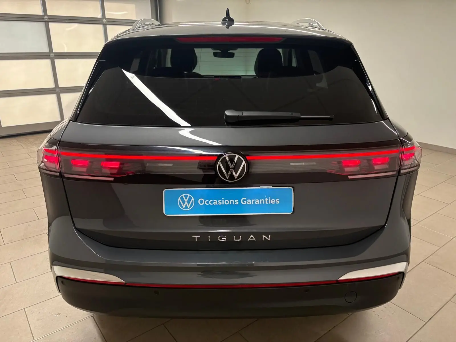 Vue arrière du Volkswagen Tiguan 2025 gris dauphin avec feux LED allumés et logo VW bien visible.