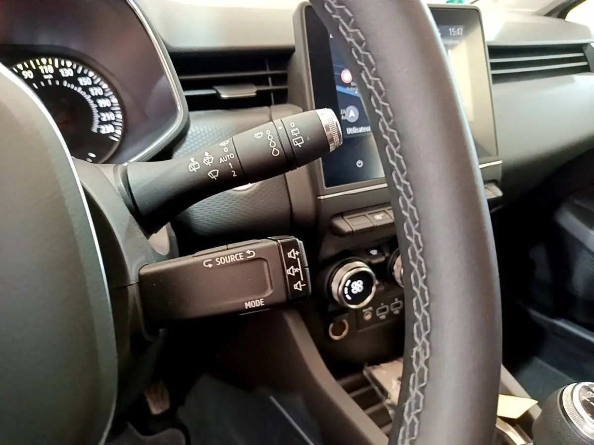 Vue intérieure rapprochée du volant gris clair de la Renault Clio Business avec commandes au volant et écran tactile visible.