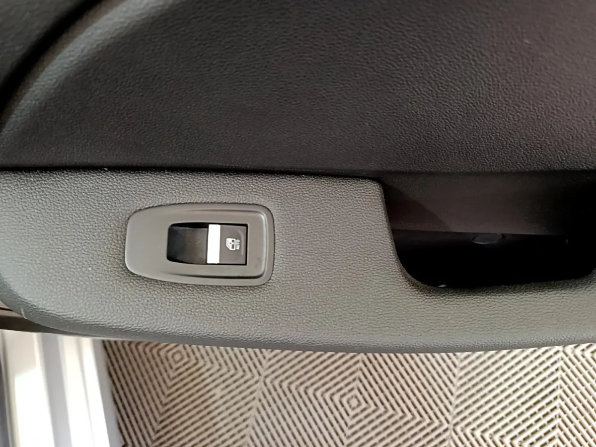 Gros plan sur le bouton de commande de lève-vitre sur la porte intérieure d’une Renault Clio Business gris clair.