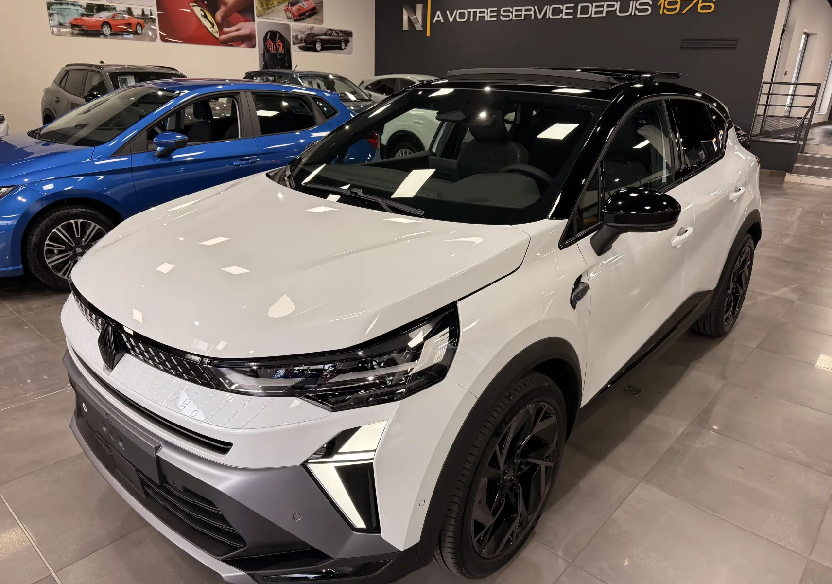Vue 3/4 avant droite du Renault Captur E-Tech blanc nacré avec toit noir et jantes noires en showroom.
