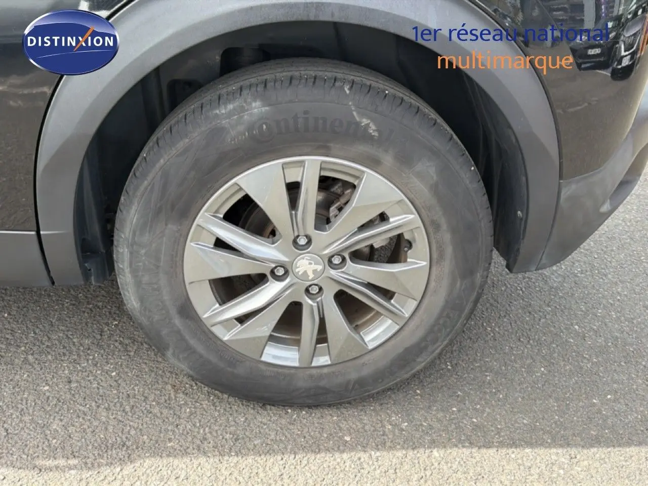 Gros plan sur la roue avant gauche d'un Peugeot 2008 noir perle métal, avec jante alliage et logo lion visible.