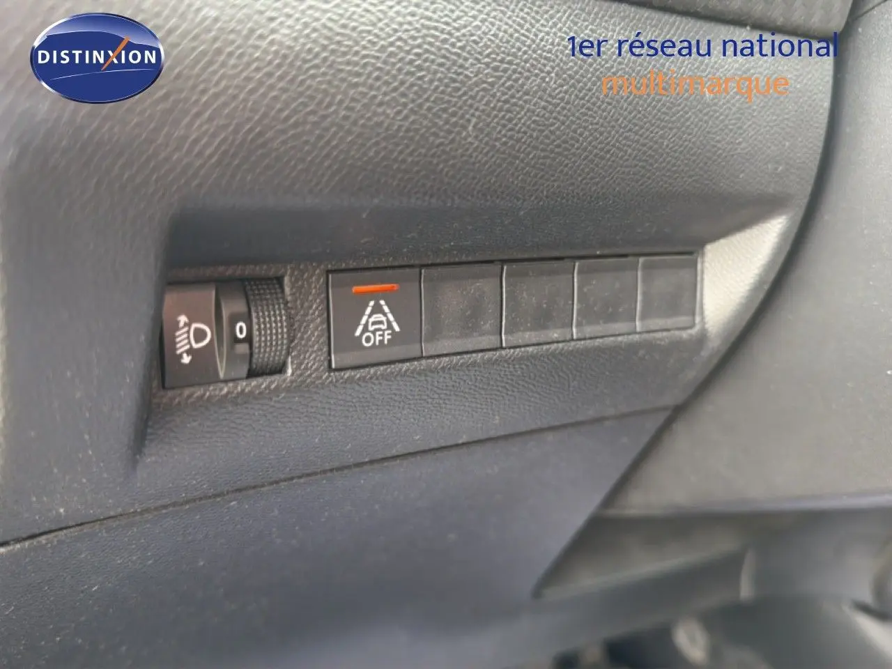 Gros plan sur les commandes de réglage des phares et de désactivation de l'alerte de franchissement de ligne dans un Peugeot 2008 noir perle 2022.