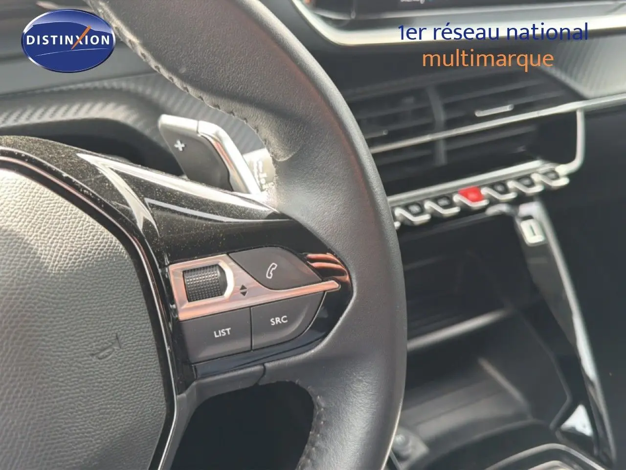 Gros plan sur le volant noir et les commandes multimédia d’un Peugeot 2008 2022, intérieur moderne avec tableau de bord noir brillant.