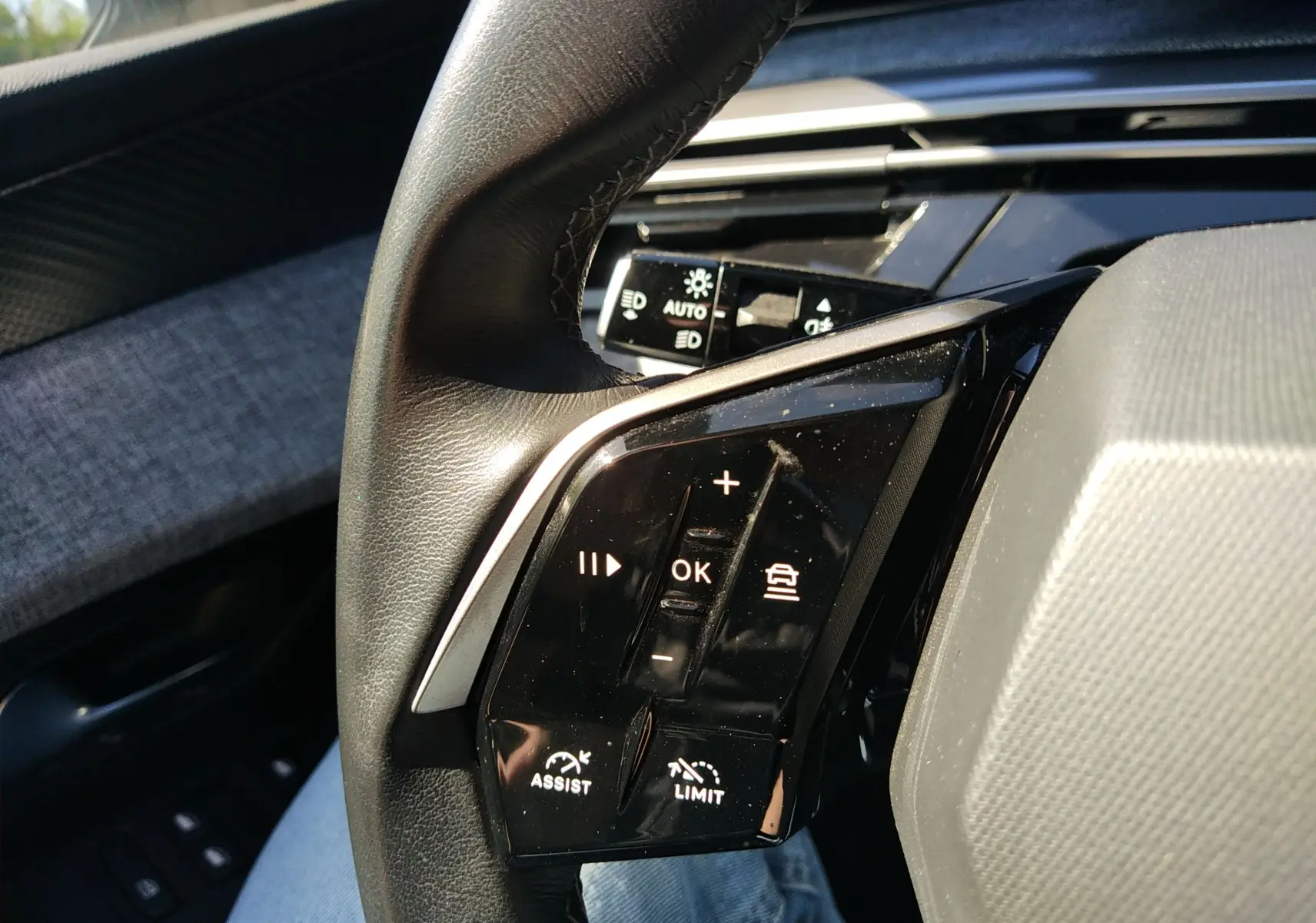 Gros plan sur les commandes au volant noir du Peugeot 3008 Hybrid 136 Allure, avec boutons de réglage et assistance.