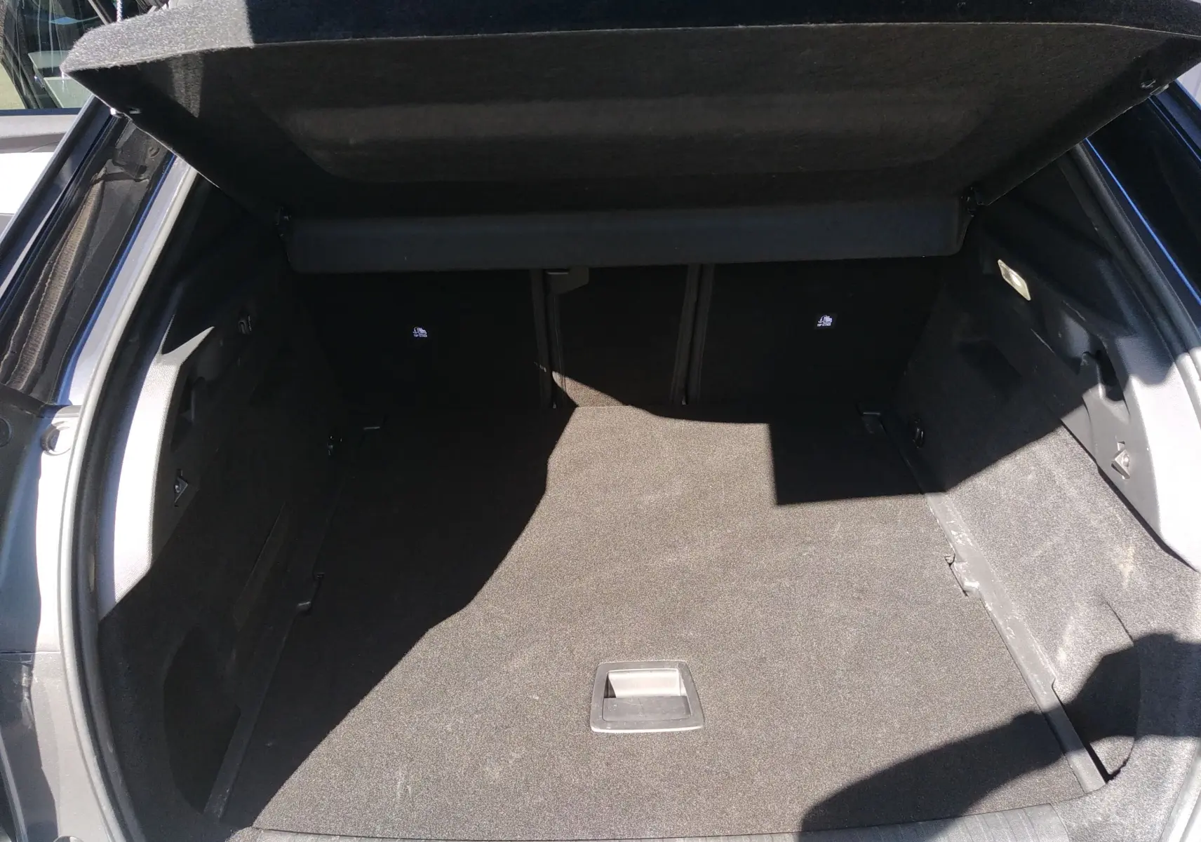 Coffre ouvert vu de l'arrière d'un Peugeot 3008 Nouveau Hybrid 136 gris titane, montrant un espace de chargement vide.