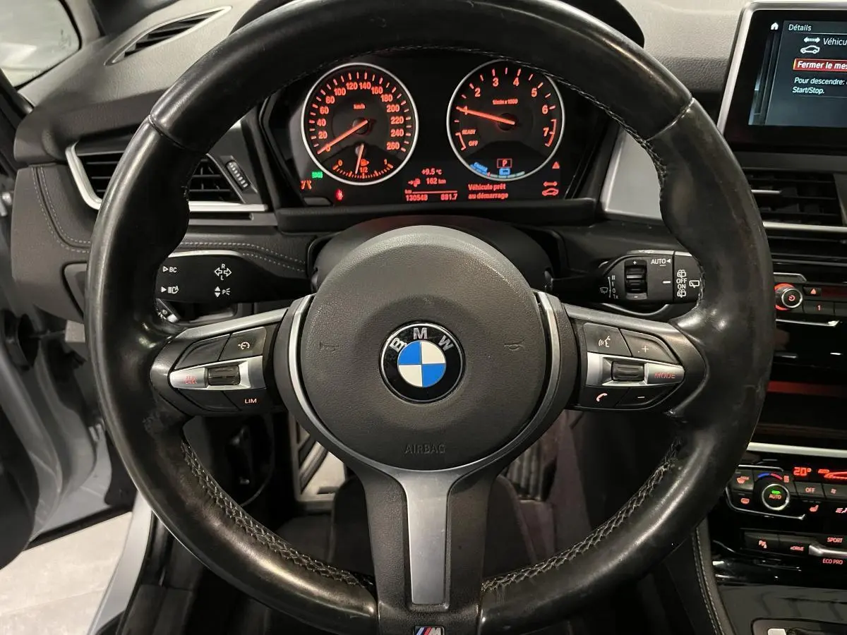 Vue intérieure centrée sur le volant M cuir noir de la BMW Série 2 225xe Active Tourer avec tableau de bord et écran multimédia allumés.