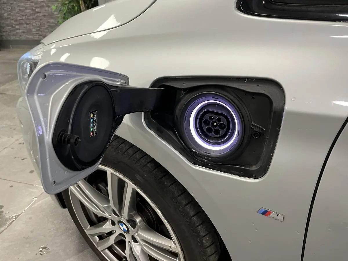 Prise de recharge ouverte côté gauche d’une BMW Série 2 225xe Active Tourer gris avec jante alliage et logo M visible.